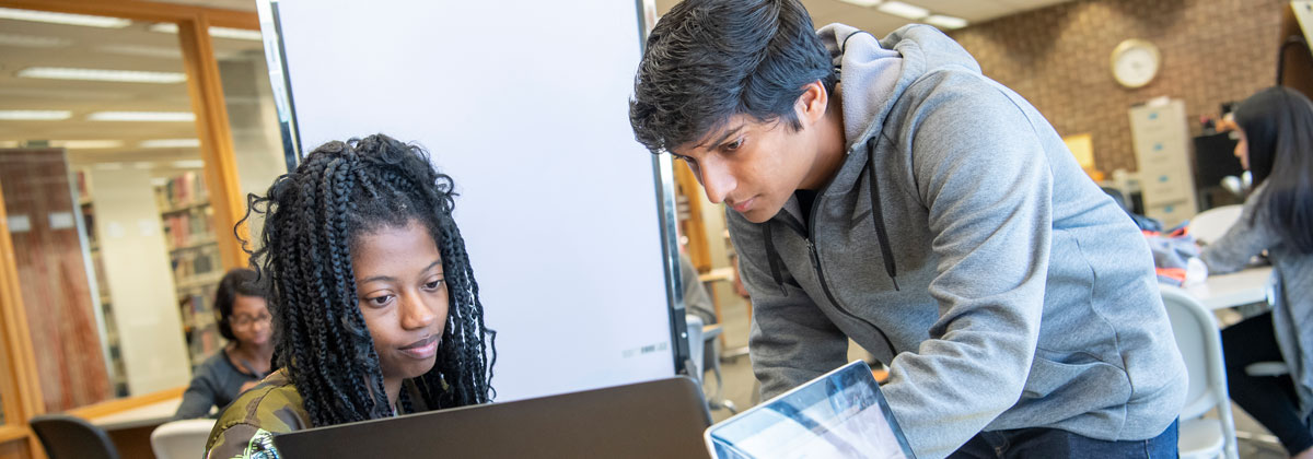 NIU student helping another student who is working on a laptop.